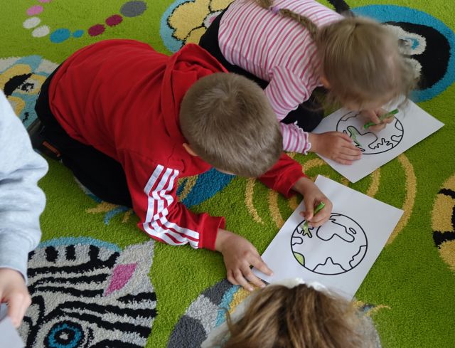 chłopiec i dziewczynka leżący na dywanie kolorują polanetę Ziemię