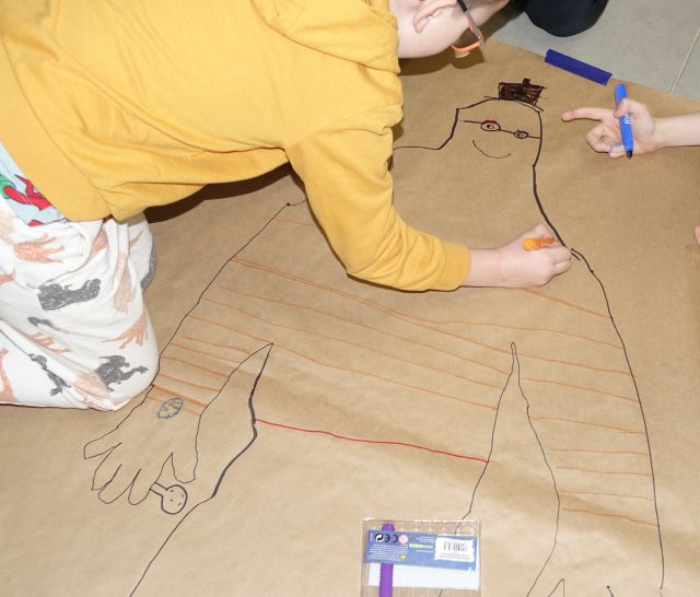 dziewczynka koloruje odrysowaną postać na dużym szarym papierze