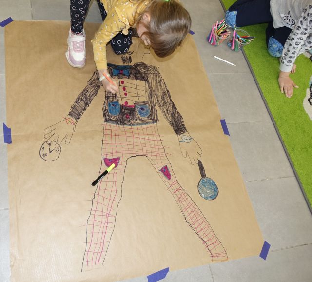 dłoż dziecka koloruje odrysowaną na szarym papierze postać