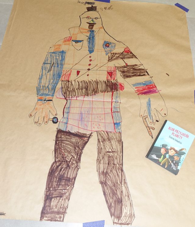 pokolorowana postać na szarym papierze, obok leży książka