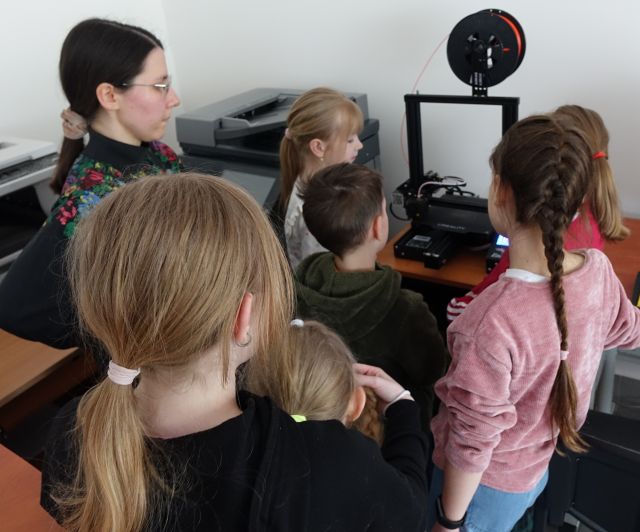 6 dzieci i biblioterka stoją przed drukarką 3d