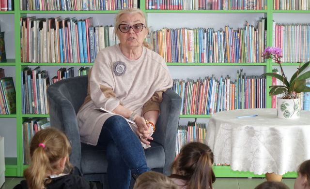 na zdjęciu autorka książki siedząca na fotelu, w tle regały z książkami