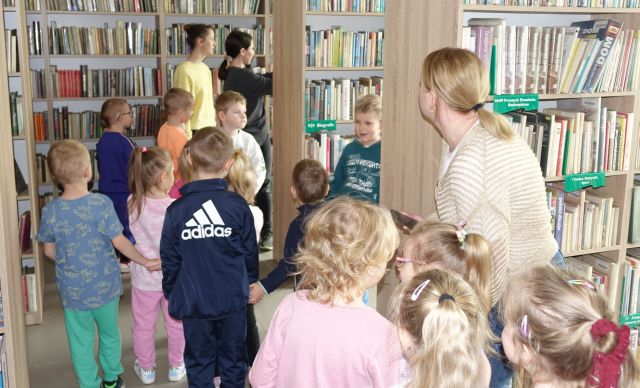 przedszkolaki z nauczycielkami spacerują między regałąmi z książkami