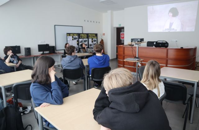 młodzież siedząca przy stolikach ogląda film wyświetlany na ścianie