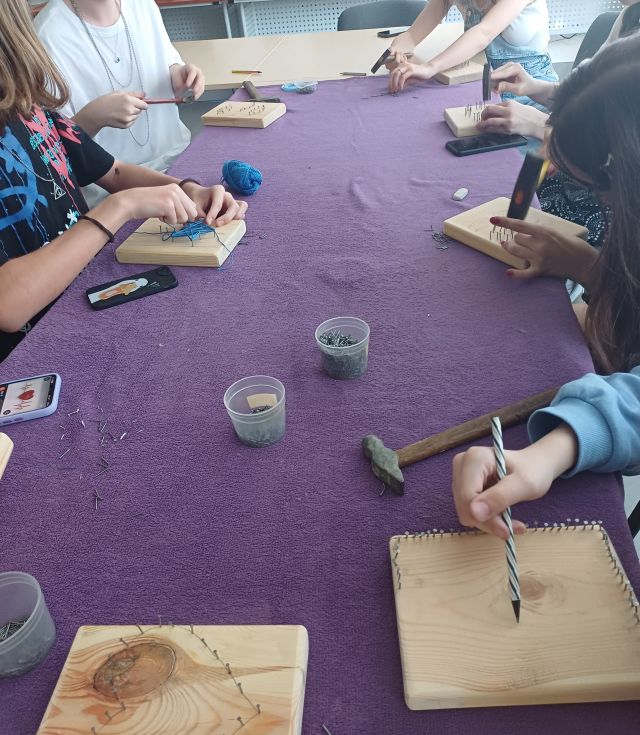 młodzież wbija gwoździe w deseczki i plącze na nich nitki tworząc różne wzory