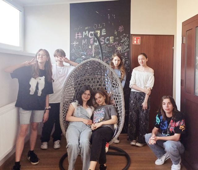 2 dziewczyny siedzą w bujanym fotelu, za nimi stoją 4 dziewczyny i chłopak