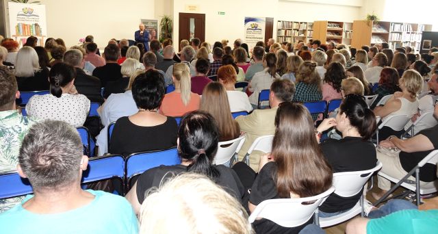 uczestnicy spotkania siedzący na krzesłach, przed nimi stojący aktor w niebieskim garniturze