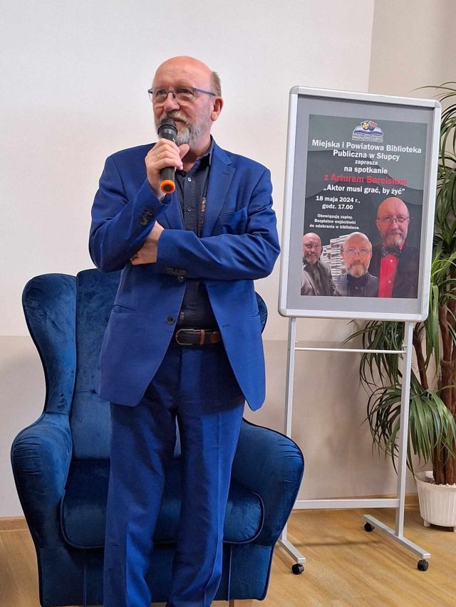 aktor w niebieskim garniturze stojący z mikrofonem