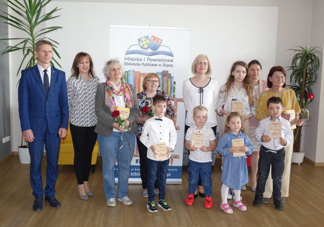 najaktywniejsi czytelnicy roku 2023 z burmistrzem i bibliotekarkami pozują do zdjęcia z dyplomami i czerwonymi różami
