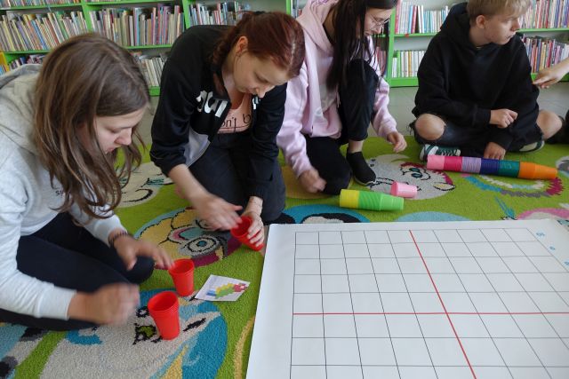 młodzież układa kolorowe kubeczki na macie