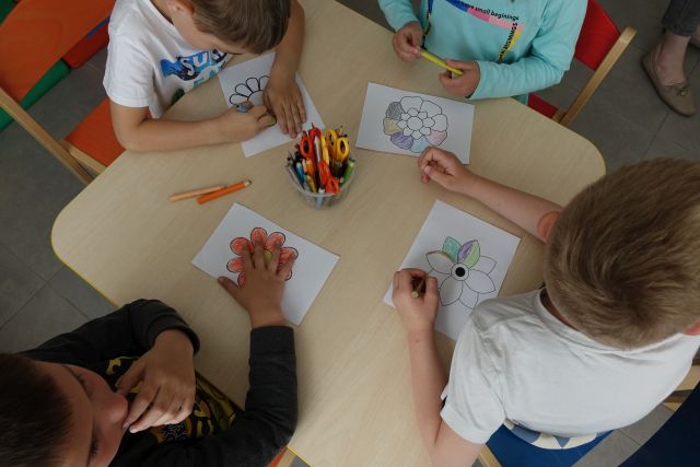 dzieci kolorują naszkicowane na kartkach kwiatki