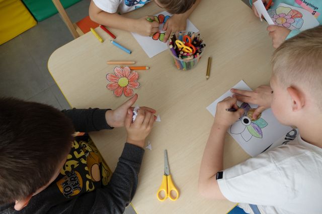 dzieci kolorują naszkicowane na kartkach kwiatki i wycinają je