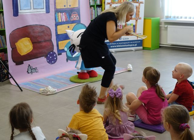 kobieta popisuje się przed dziećmi z rodzicami siedzącymi na pufach i krzesłach