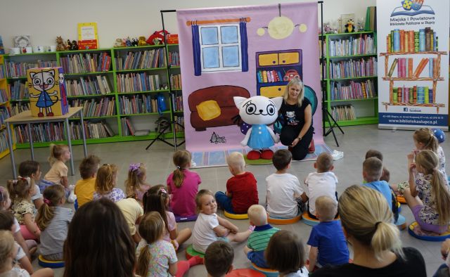 animatorka przytula dużą maskotkę Kici Koci, przed niąsiedzą na podłodze dzieci