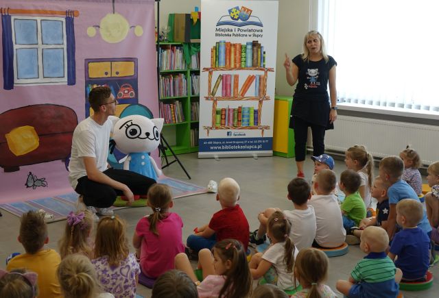 mężczyzna kuca przy maskotce Kici Koci, animatorka opowiada siedzącym dzieciom