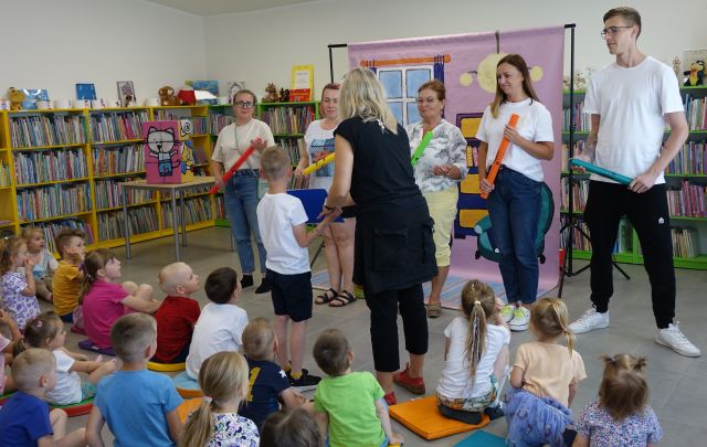 6 dorosłych dzieci gra na bum bum rurkach, chłopiec z animatorką pokazują nuty, pozostałę dzieci siedzą