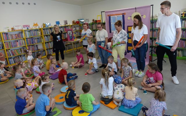 6 dorosłych osób gra na bum bum rurkach, 6 dzieci siedzących na podłodze gra na dzwonkach