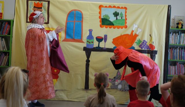 aktor przebrany za kota w butach i drugi przebrany za hrabiego rozmawiają, w tle plansza przedstawiająca komnatę