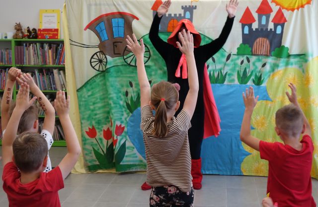 aktor przebrany za kota w butach stoi z podniesionymi rękami, przed nim stoją dzieci z podniesionymi rękami