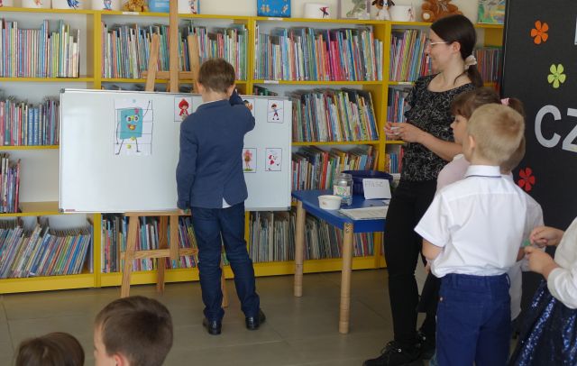 chłopiec przykleja do tablicy magnetycznej obrazek, pozostałę przedszkolaki stoją i siedzą na dywanie