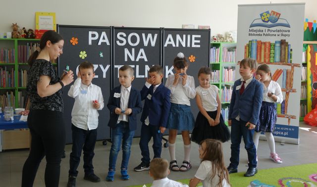 7 przedszkolaków stoi w rządku przed bibliotekarką