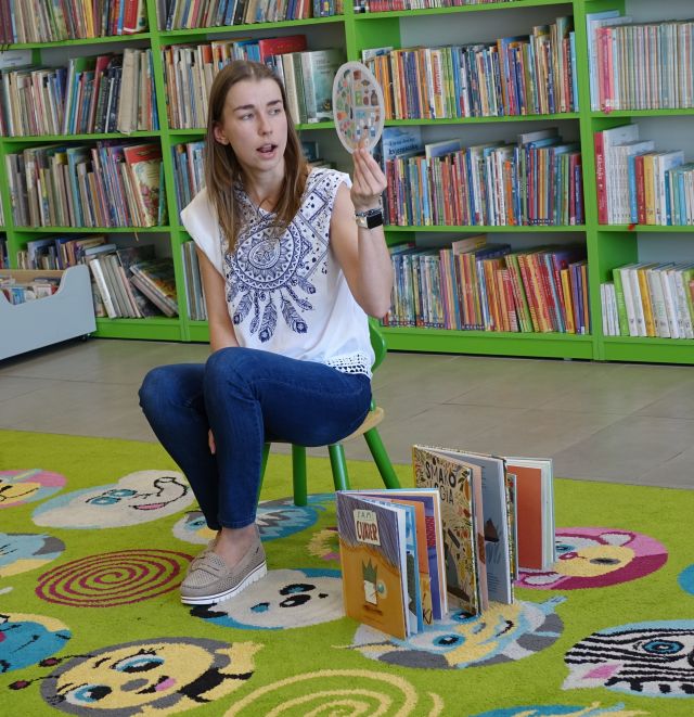 kobieta pokazuje dzieciom siedzącym na kolorowym dywanie zdrowy talerz