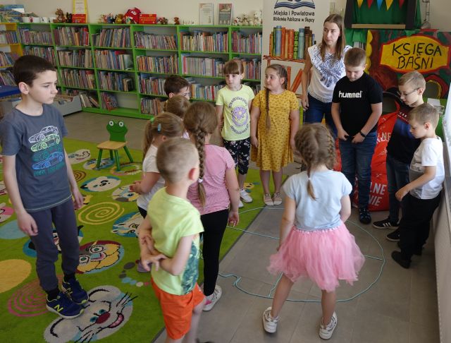 dzieci i kobieta stoją w kułeczku, w tle regały z książkami