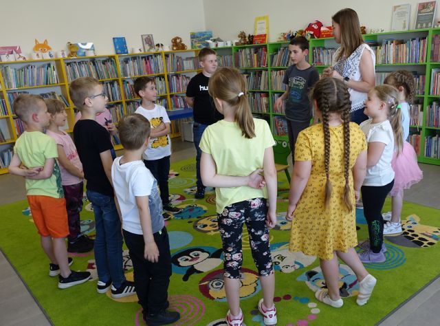 dzieci i kobieta stoją w kółku na kolorowym dywanie