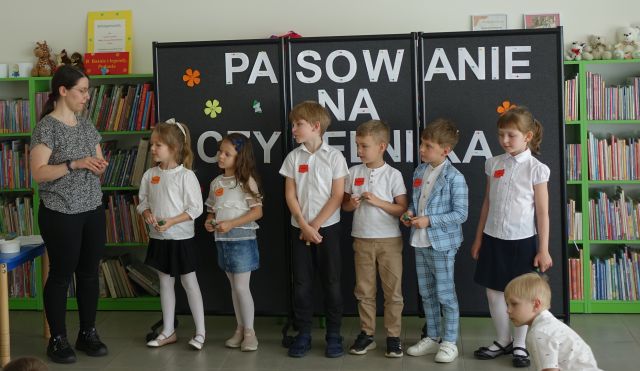6 dzieci stoi w rządku przed bibliotekarką