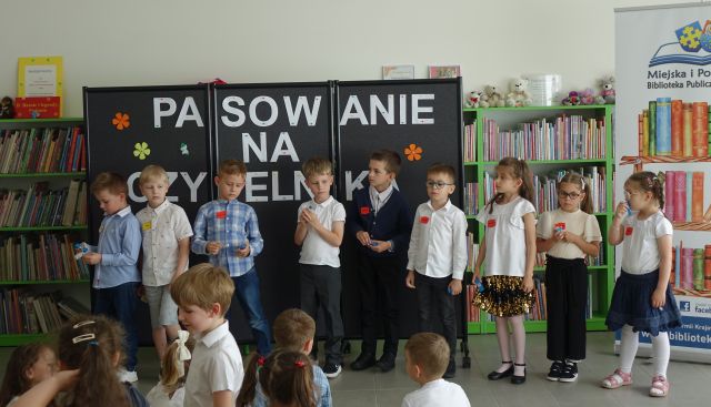 10 dzieci stoi w rzędzie przed bibliotekarką