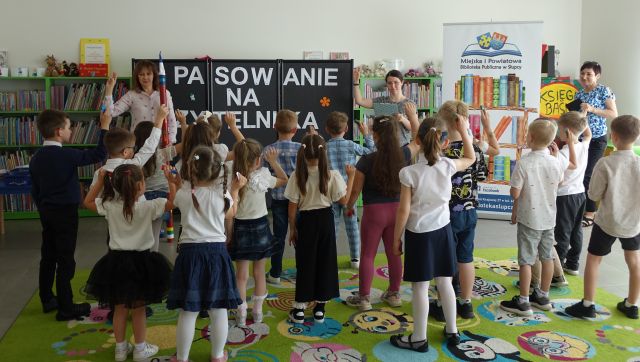 dzieci i 2 kobiety stoją z podniesionymi do góry prawymi rękami