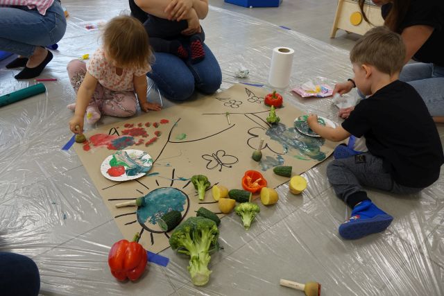 dzieci z mamusiami poznają warzywa i maluja farbami na dużym arkuszu papieru