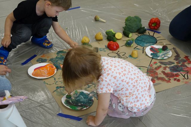 dzieci malują na rozłożonej na podłodze tekturze, obok leżą różne warzywa