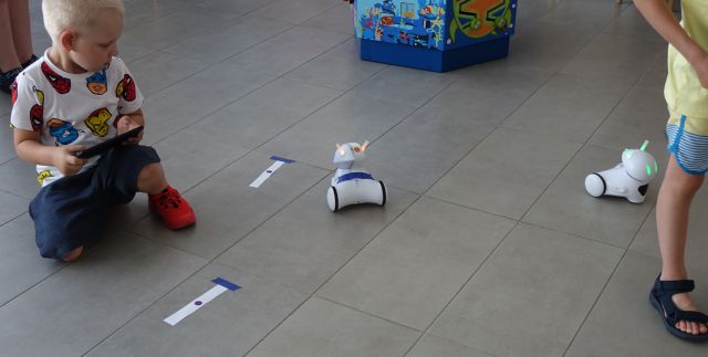 chłopiec trzyma w rękach tablet, na podłodze 2 roboty Photon