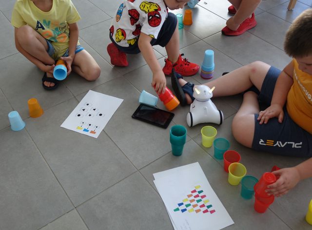 dzieci układają kolorowe kubeczki według wzoru rozrysowanego na kartkach