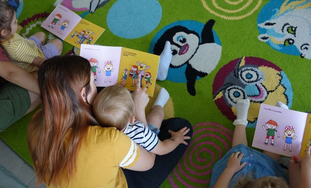 mamy trzymają dzieci na kolanach i pokazują im książeczki