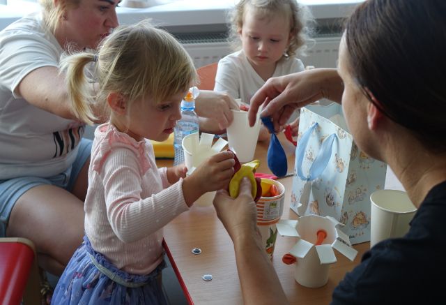 dzieci i mamy wkładają kolorowe balony do papierowych kubeczków