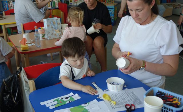 dzieci z mamami siedzą przy stolikach i kolorują papierowe kubeczki