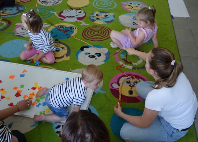 małe dzieci z mamami nawlekają makaron penne na sznurki