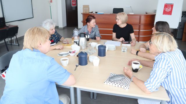 6 kobiet rozmawia siedząc przy połączonych w kwadrat stołach