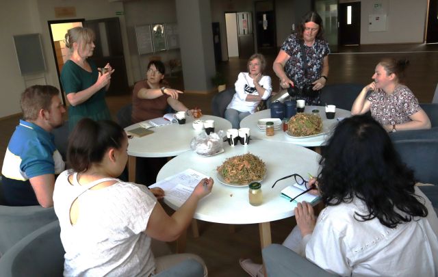 uczestnicy spotkanie siedzą przy białych okrągłych stołach, na stołach zioła i kubki