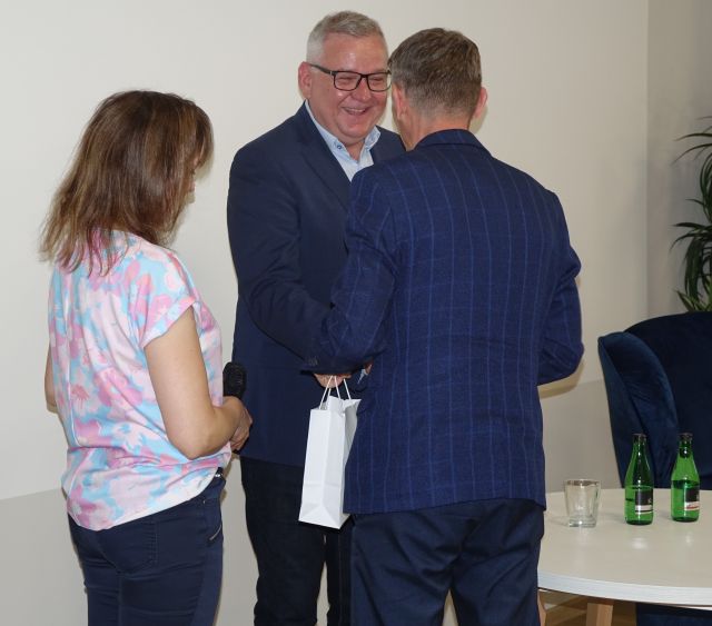 kobieta i mężczyzna stojący tyłem do aparatu wręczają prezent gościowi