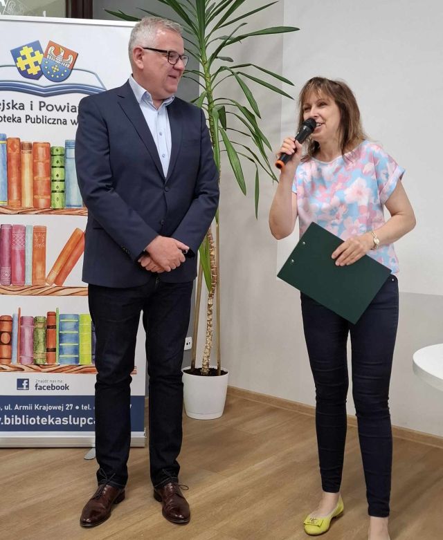dyrektorka biblioteki z mikrofonem, obok po lewej stronie stoi mężczyzna w garniturze