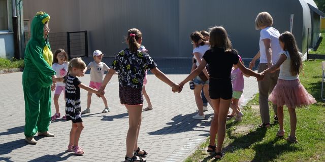 dzieci i kobieta przebrana za żabę trzymając się za ręce chodzą w kółko