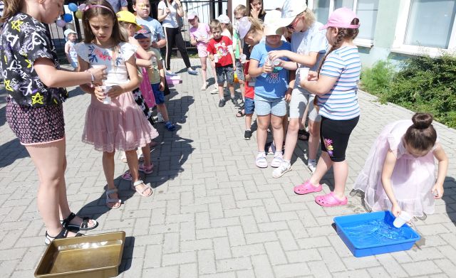 dzieci stoją w dwóch rzędach trzymając w dłoniach plastikowe kubeczki