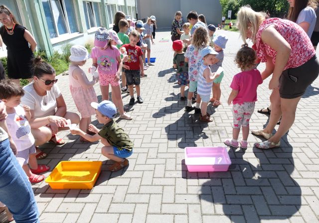 dzieci stoją w dwóch rzędach z kubeczkami plastikowymi, przed nimi miski z wodą