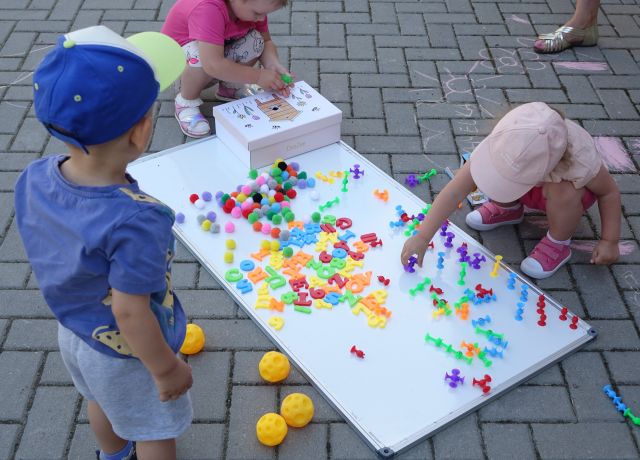3 małych dzieci przykleja do tablicy magnetycznej małę kolorowe piłeczki