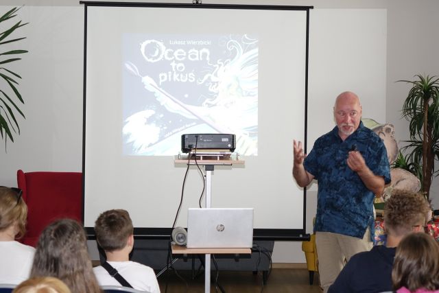 na zdjęciu autor opowiadający dzieciom siedzącym na krzesłach