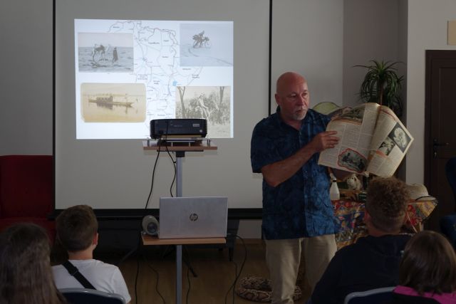 mężczyzna stojący przed dziećmi pokazuje starą gazetę