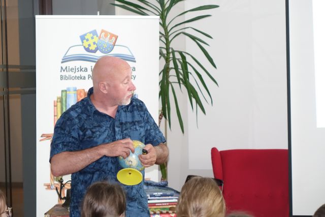 mężczyzna pokazuje siedzącym dzieciom globus